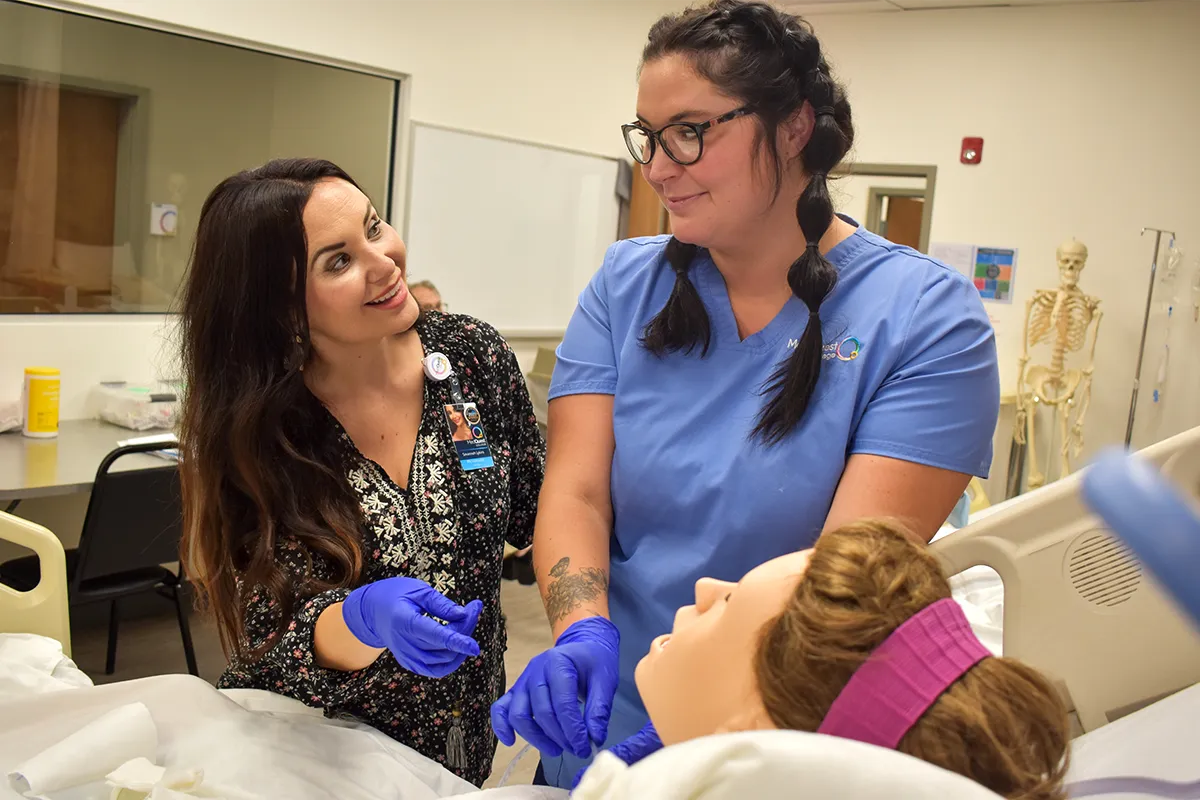 nursing teacher and student working together with a mannequin